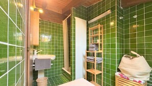 Un bagno con una vasca, uno scaffale in legno con asciugamani e una parete rivestita di piastrelle verdi.