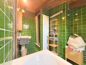Un baño con una bañera, un estante de madera con toallas y una pared con azulejos verdes.