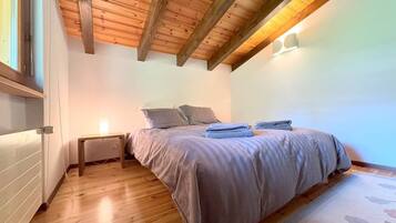 Ein Schlafzimmer mit Holzboden, einem Bett mit grauer Bettwäsche, einem Nachttisch mit Lampe und einem Fenster.