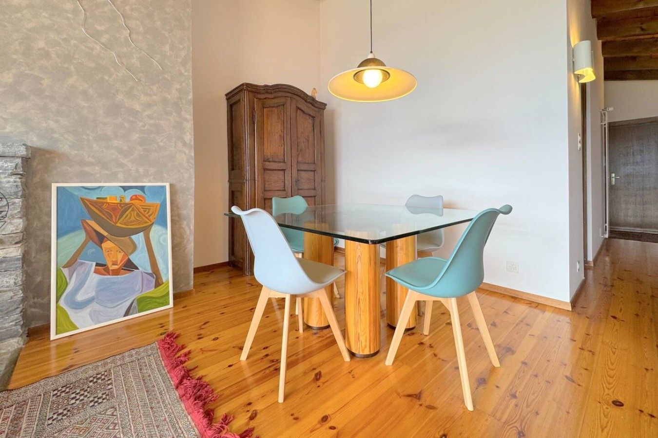 Un comedor con mesa de vidrio, dos sillas, un aparador de madera y una lámpara colgante.
