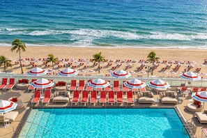 Ein Poolbereich mit Liegestühlen und Sonnenschirmen, ein Strand mit Stühlen und Sonnenschirmen sowie ein freier Blick auf den Ozean.