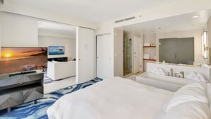 Ein Hotelzimmer mit einem Bett, einem Fernseher, der einen Sonnenuntergang zeigt, einem Badezimmer mit Dusche und einem großen Spiegel.