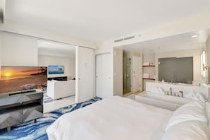 Hotelkamer met een bed, een televisie waarop een zonsondergang te zien is, een badkamer met douche en een grote spiegel.