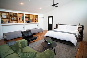 A modern bedroom with a bed, a seating area with a sofa and chair, a small table, and a wall with shelves displaying trophies and awards. - Mid Mod Studio - Garage - 0.5 mi UCA (Conway)