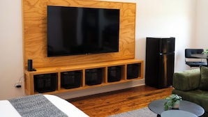 A modern living room with a mounted flat-screen TV, a black refrigerator, and a seating area with a green sofa and a small round table.