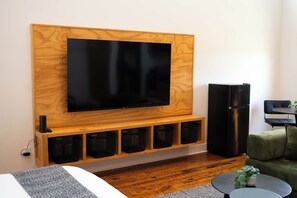 A modern living room with a mounted flat-screen TV, a black refrigerator, and a seating area with a green sofa and a small round table.