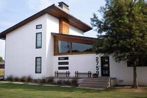 A modern two-story house with a white exterior, large windows, and a wooden roof.