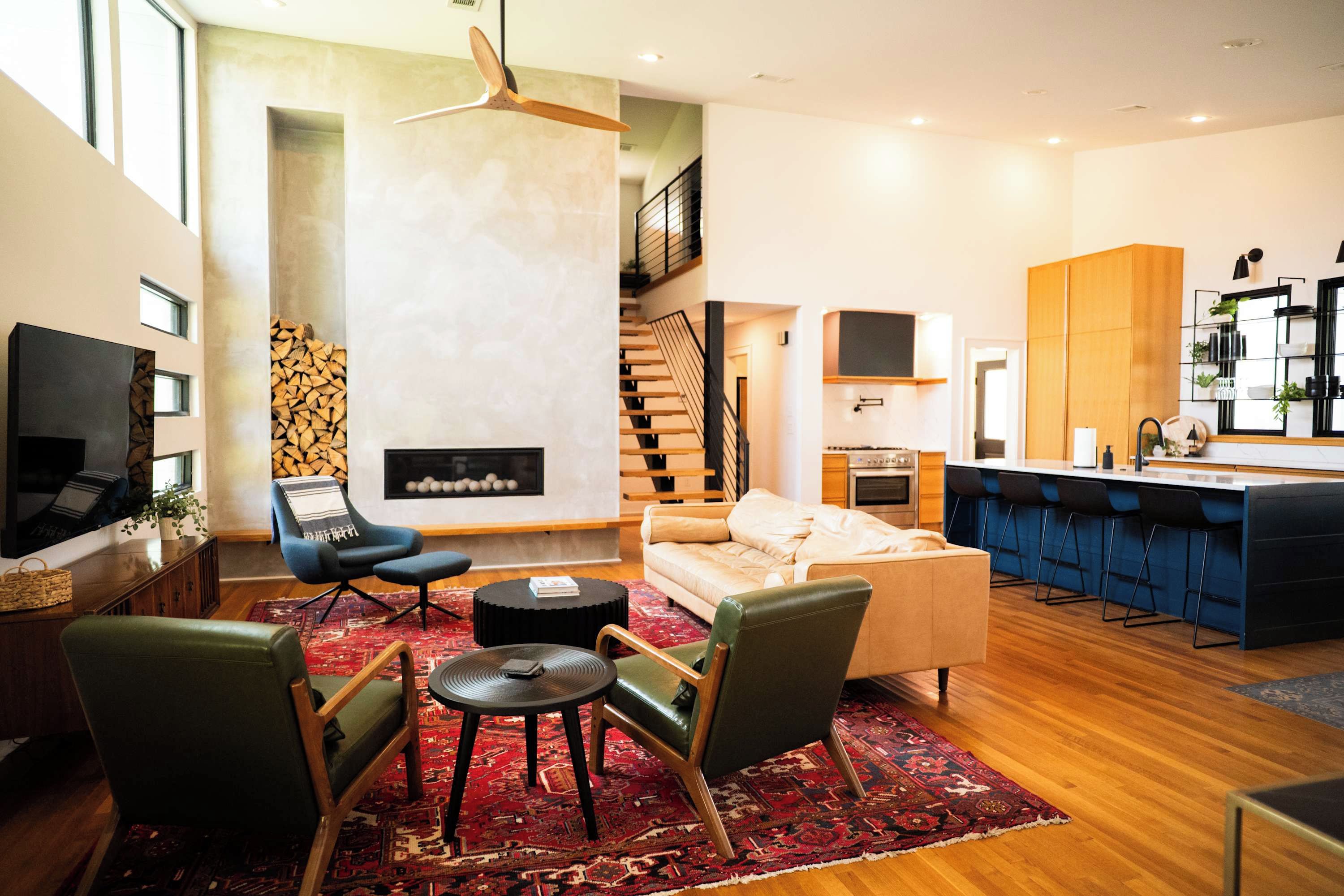 A modern living room with a fireplace, a kitchen area, and a staircase.
