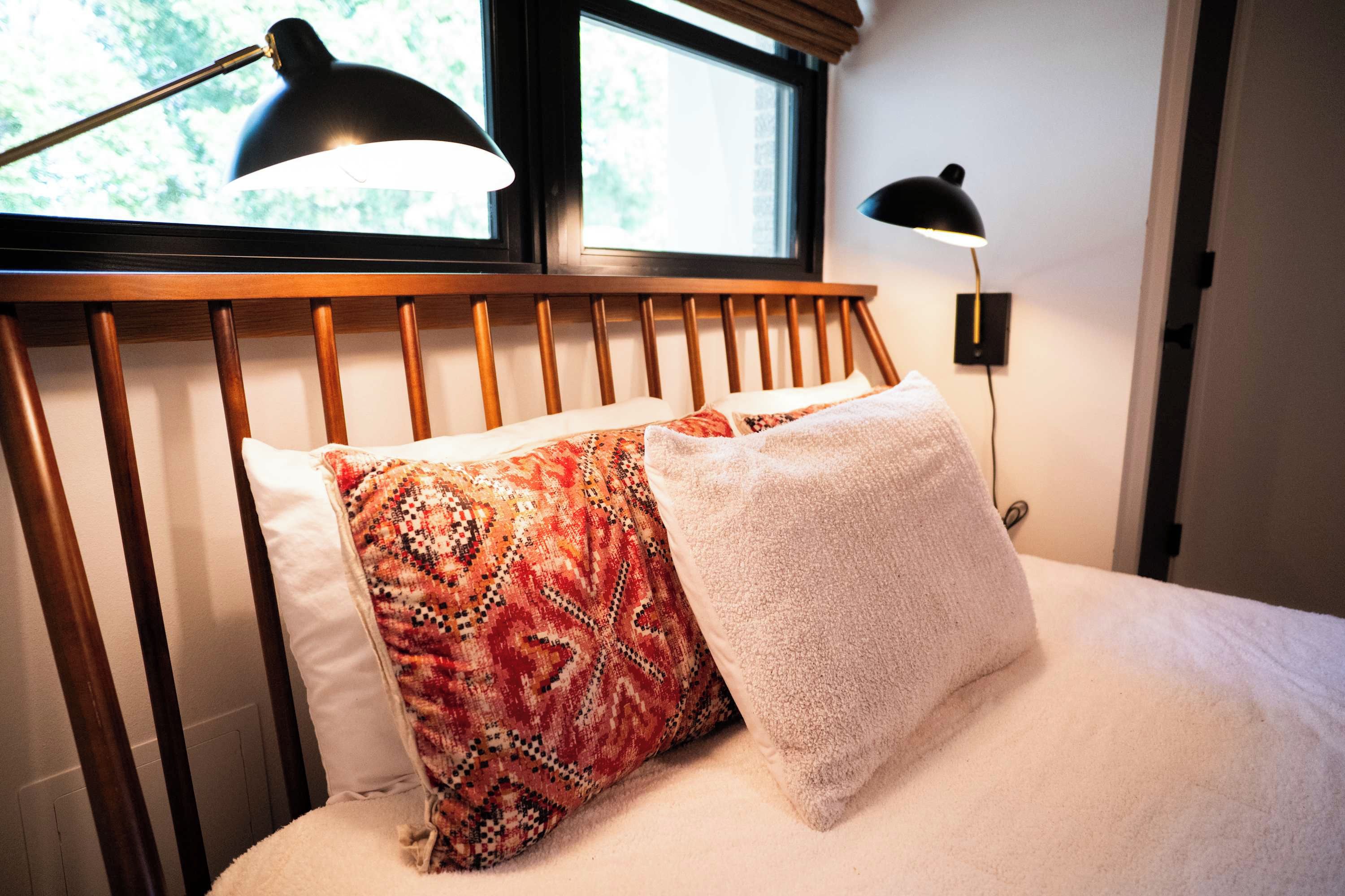 Una cama con cabecera de madera, dos almohadas y una lámpara de noche.