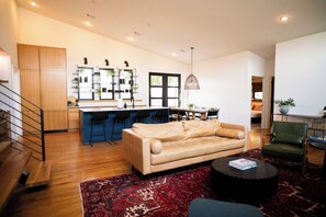A modern living room with a sofa, a coffee table, and a rug. There is a kitchen area with a bar and chairs. - Mid Mod Lodge - Patio - Office - 0.5 mi UCA (Conway)