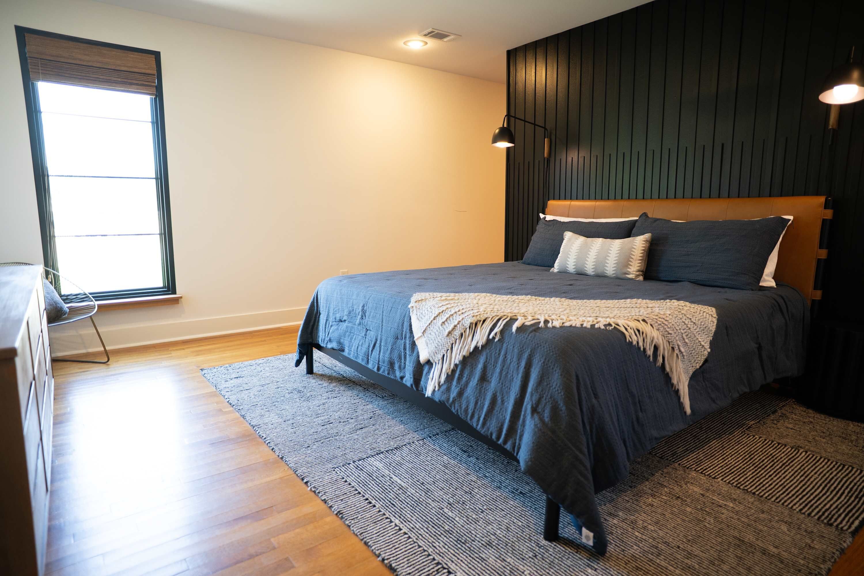 Een slaapkamer met een bed, een raam, een wandlamp en een houten vloer.