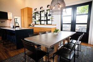 A modern kitchen with a central island, black chairs, and a hanging light fixture. - Mid Mod Lodge - Central Location - 0.5 mi UCA (Conway)