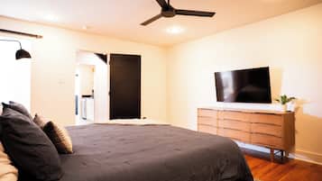 A bedroom with a bed, a ceiling fan, a TV on a dresser, and a door leading to another room.