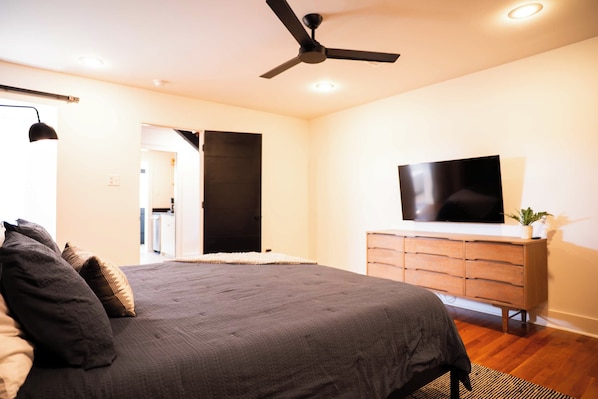 A bedroom with a bed, a ceiling fan, a TV on a dresser, and a door leading to another room.