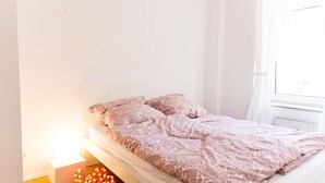 Ein schlicht eingerichtetes Schlafzimmer mit Bett, Nachttisch und Fenster.