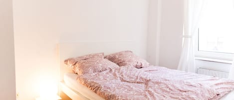 Ein schlicht eingerichtetes Schlafzimmer mit Bett, Nachttisch und Fenster.