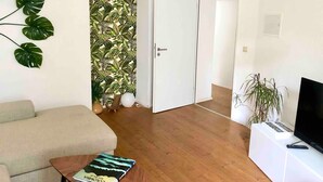 Ein Wohnzimmer mit einer Couch, einem Couchtisch mit einem Buch, einem Fernseher auf einem Schrank und einer Pflanze.