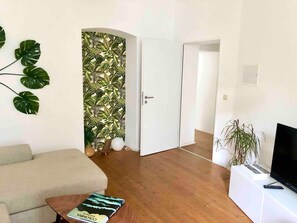 Un salon avec un canapé, une table basse sur laquelle se trouve un livre, un téléviseur posé sur un meuble et une plante.