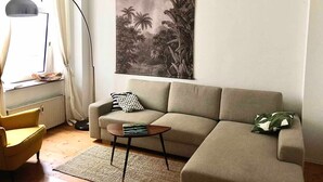 Ein Wohnzimmer mit einer Couch, einem Beistelltisch, einer Stehlampe und einem Bild von einer tropischen Szene.