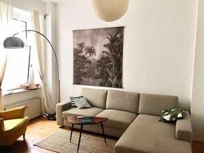 Un salon comprenant un canapé, une table d’appoint, un lampadaire et un tableau représentant un paysage tropical.