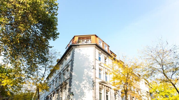 Ein Eckgebäude mit Balkon, umgeben von Bäumen mit gelben Blättern.