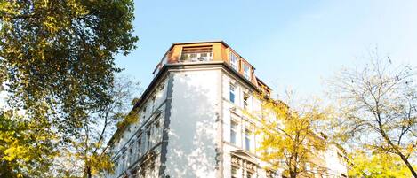 A corner building with a balcony, surrounded by trees with yellow leaves.