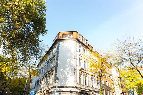 Un immeuble d’angle doté d’un balcon, entouré d’arbres aux feuilles jaunes.