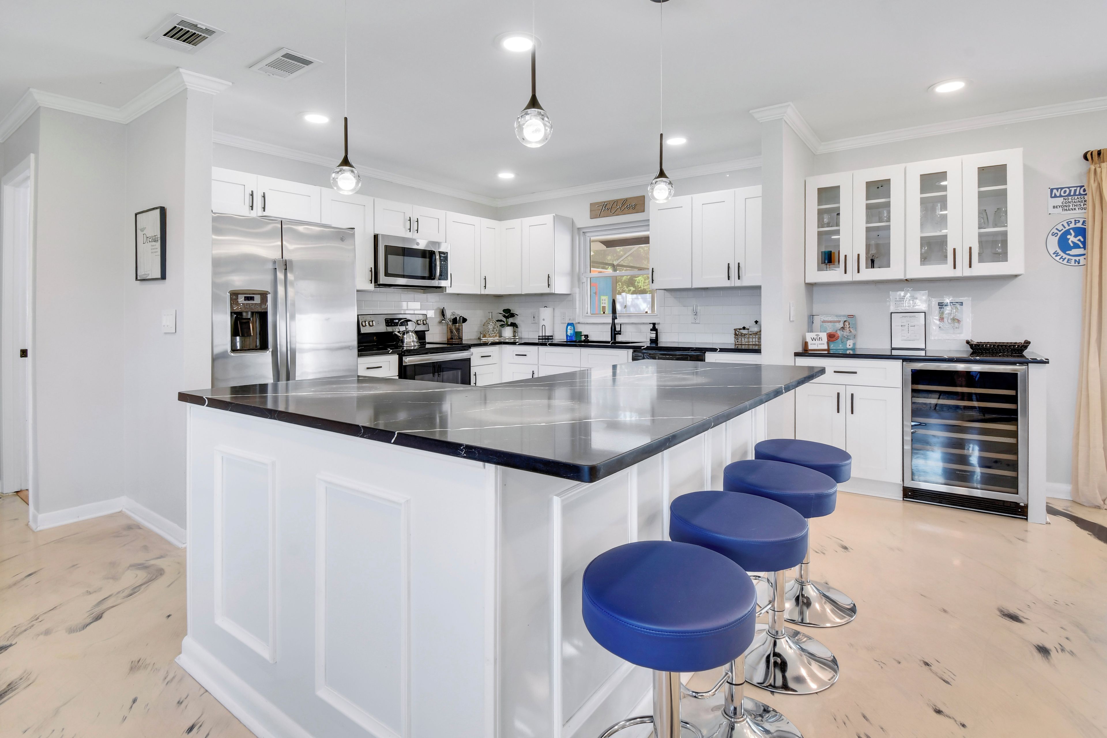 A modern kitchen with white cabinetry, a central island with bar stools, stainless steel appliances, and pendant lighting.