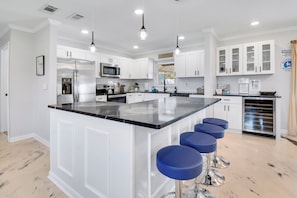 A modern kitchen with white cabinetry, a central island with bar stools, stainless steel appliances, and pendant lighting. - Heated Pool w/ Hot Tub • 10 min to Beaches • Pinellas Trail Access (Largo)