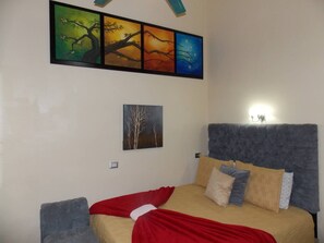 Une chambre à coucher avec un lit, une table de chevet, une lampe fixée au mur et un tableau au-dessus du lit.