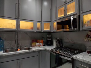Une cuisine avec des meubles de couleur grise, un évier en acier inoxydable, une cuisinière et un four à micro-ondes.