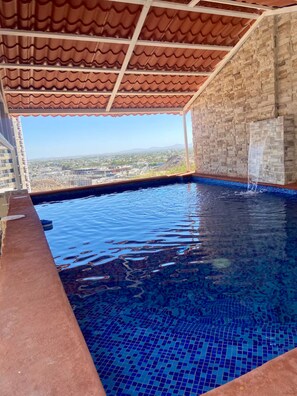 An indoor swimming pool with a tiled floor, a view of a cityscape, and a stone wall. - Whale Hill Family Duplex, Units A & B (Puerto Peñasco)