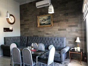 A modern living room with a grey sofa, a dining table with chairs, a clock, an air conditioner, a framed picture, and a lamp. - Whale Hill Family Duplex, Units A & B (Puerto Peñasco)