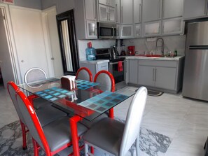 A modern kitchen with white cabinets, a stainless steel refrigerator, and a glass dining table with red chairs. - Whale Hill Family Duplex, Units A & B (Puerto Peñasco)