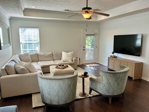 A living room with a sectional sofa, two armchairs, a television, and a ceiling fan.