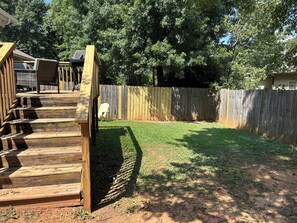 Ein Garten mit Holzterrasse, umzäunter Fläche und Rasen.