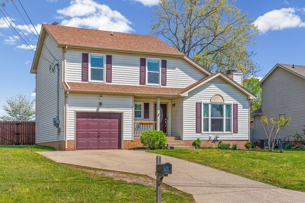 A two-story house with a front garage, a small porch, and a well-maintained lawn.