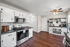 A modern kitchen with white cabinetry, stainless steel appliances, and a wooden floor.