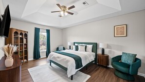 A bedroom with a bed, a chair, a television, a ceiling fan, and a window with curtains. - Relax & Recharge  Cozy 2BR Near Fort Campbell (Clarksville)