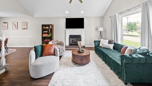 A spacious living room with a fireplace, a large green sofa, a round coffee table, and a ceiling fan. - Relax & Recharge  Cozy 2BR Near Fort Campbell (Clarksville)
