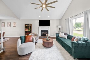 A spacious living room with a fireplace, a large green sofa, a round coffee table, and a ceiling fan.