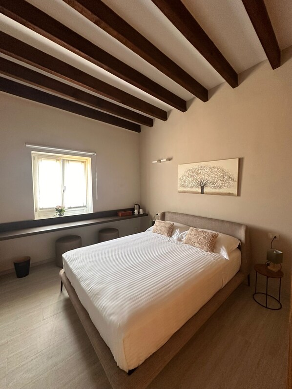 A bedroom with a large bed, a window, a painting, and a small table.