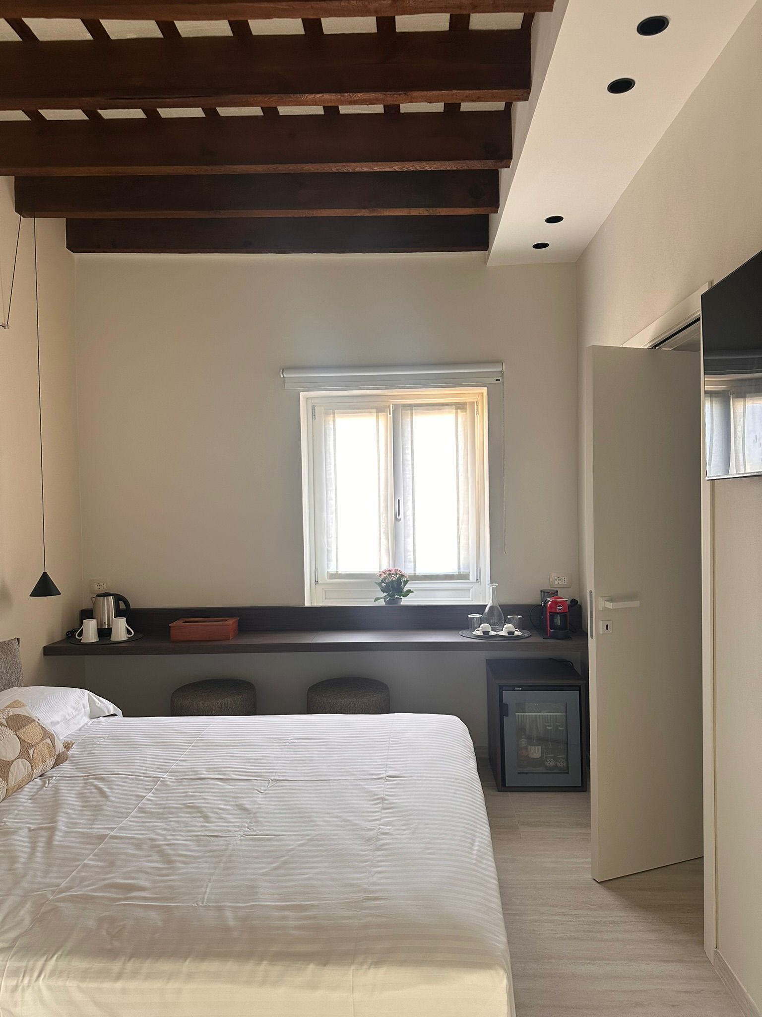 Une chambre avec un lit, un bureau avec un ordinateur, une fenêtre et un réfrigérateur.