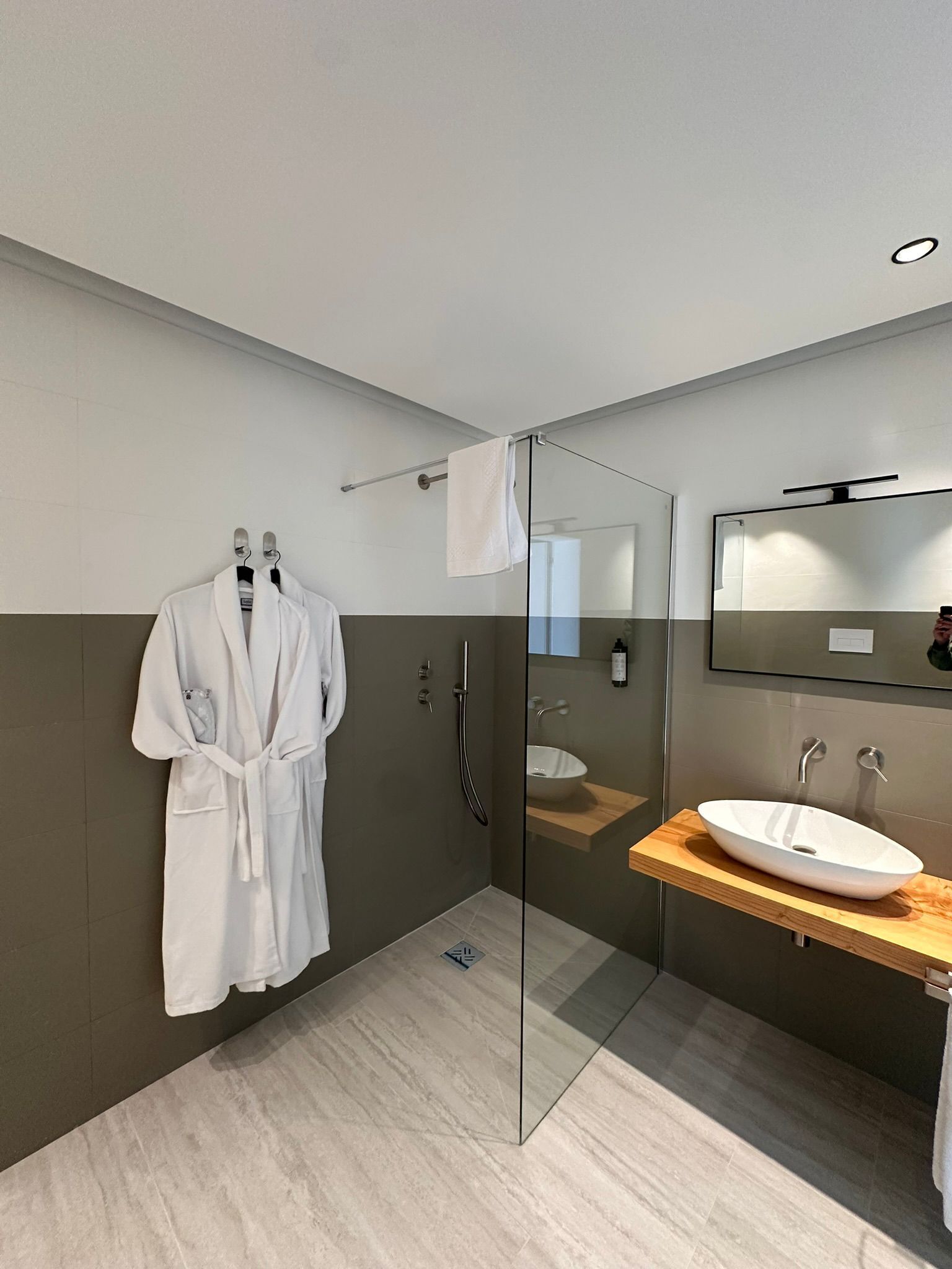 Ein modernes Badezimmer mit einer gläsernen Duschkabine, einem Holzwaschtisch mit weißem Waschbecken und einem Bademantel an einem Haken.