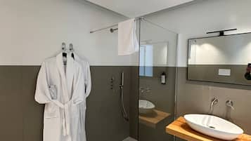 Ein modernes Badezimmer mit einer gläsernen Duschkabine, einem Holzwaschtisch mit weißem Waschbecken und einem Bademantel an einem Haken.