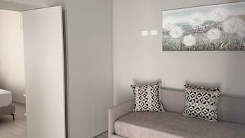 Una sala moderna con un sofá, cojines estampados, una obra de arte colgada en la pared y un armario entreabierto.