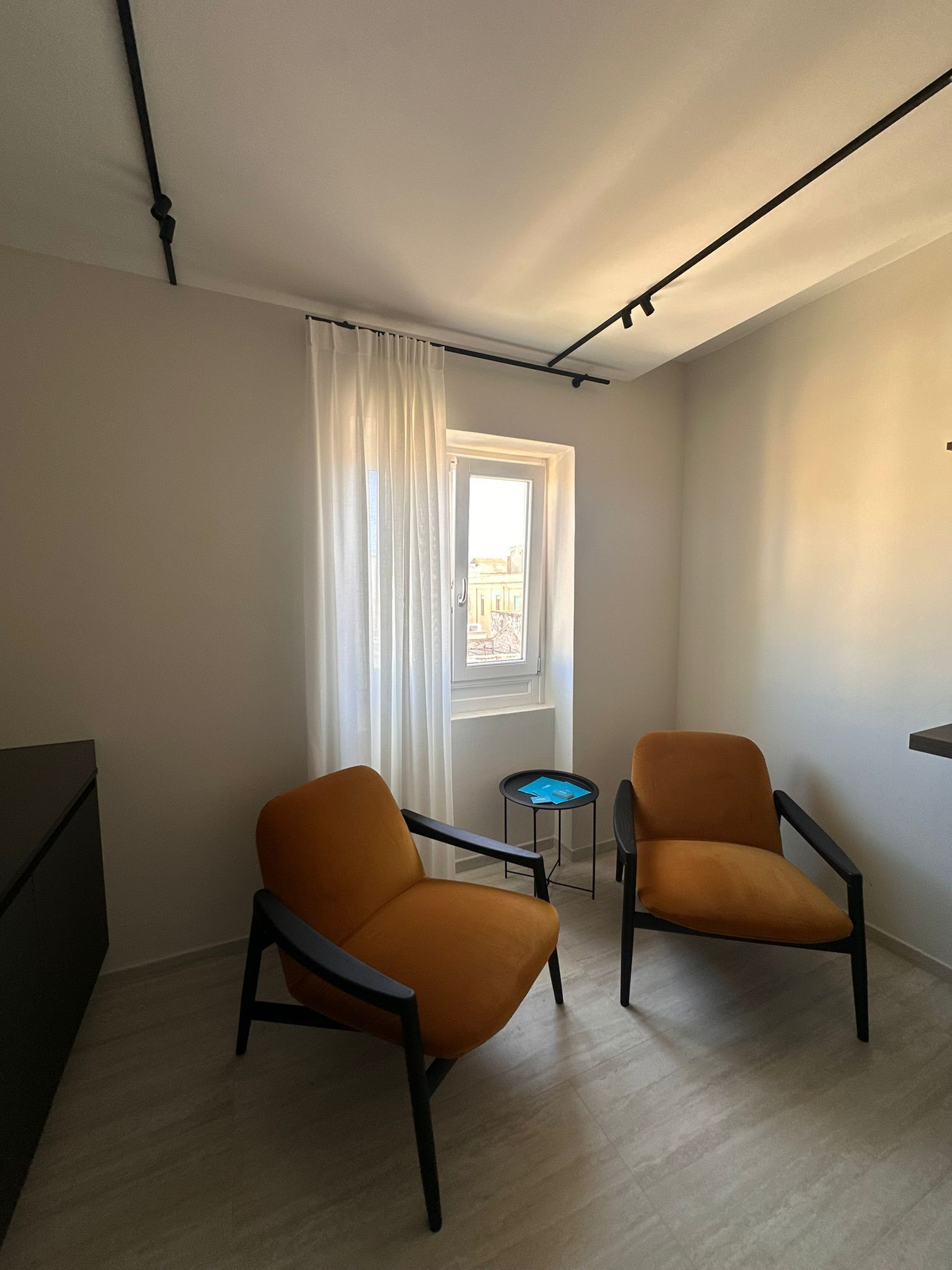 Una habitación con dos sillones, una mesita, una ventana con cortinas y vista a la calle.