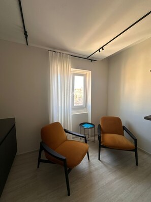 A room with two armchairs, a small table, a window with curtains, and a visible street view.