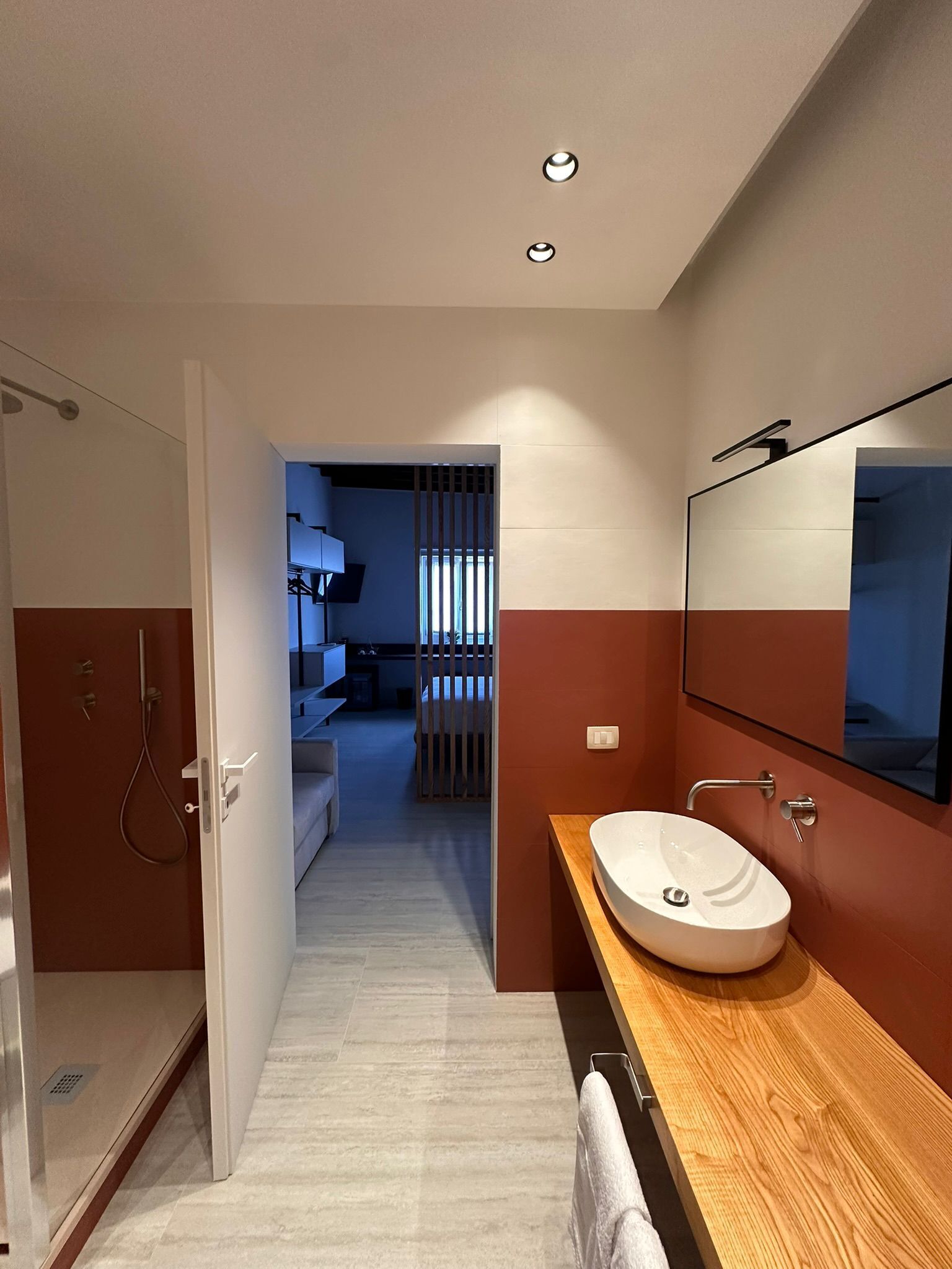 A modern bathroom with a wooden vanity, a large mirror, and a shower area.