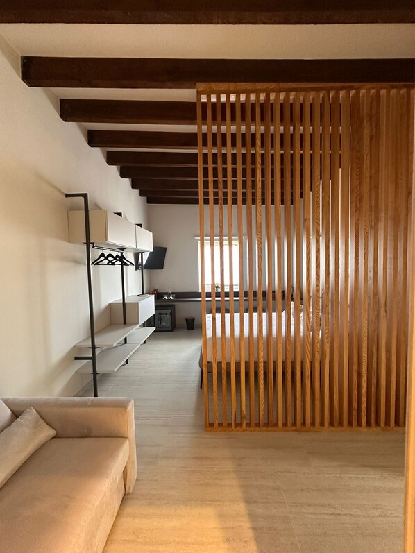 Una habitación de hotel moderna con un separador de madera, un sofá, un escritorio con una computadora y una cama.